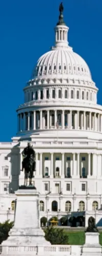 The white dome of the U.S. Capitol building with a clear blue sky and statue in front.