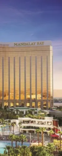 Golden Mandalay Bay hotel tower with palm trees and a large pool under a clear blue sky at sunset.