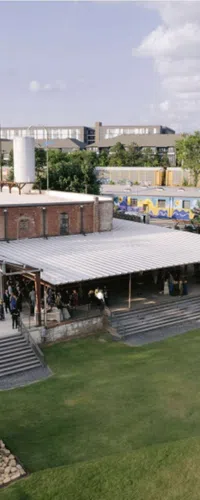 Outdoor gathering at a brick building with a covered patio and green lawn on a sunny day.