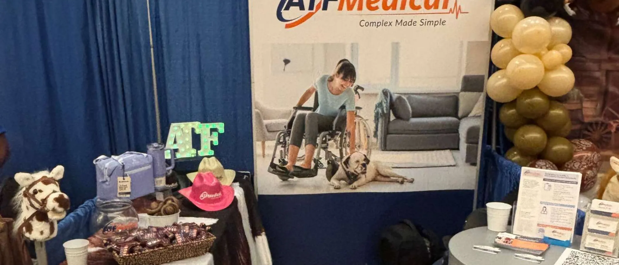 ATF Medical booth with a banner featuring a woman in a wheelchair and promotional items on a decorated table.