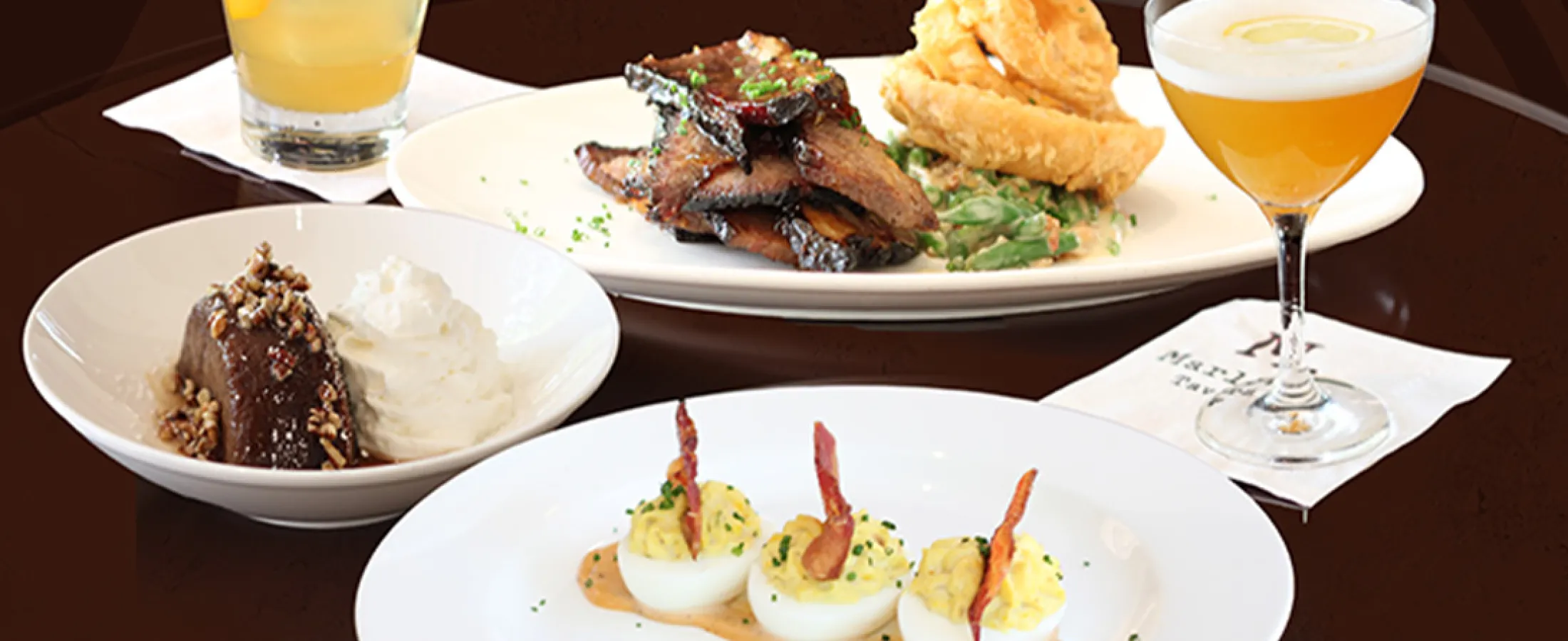 A vibrant spread of delicious dishes including salads, meats, and cocktails on a wooden table.
