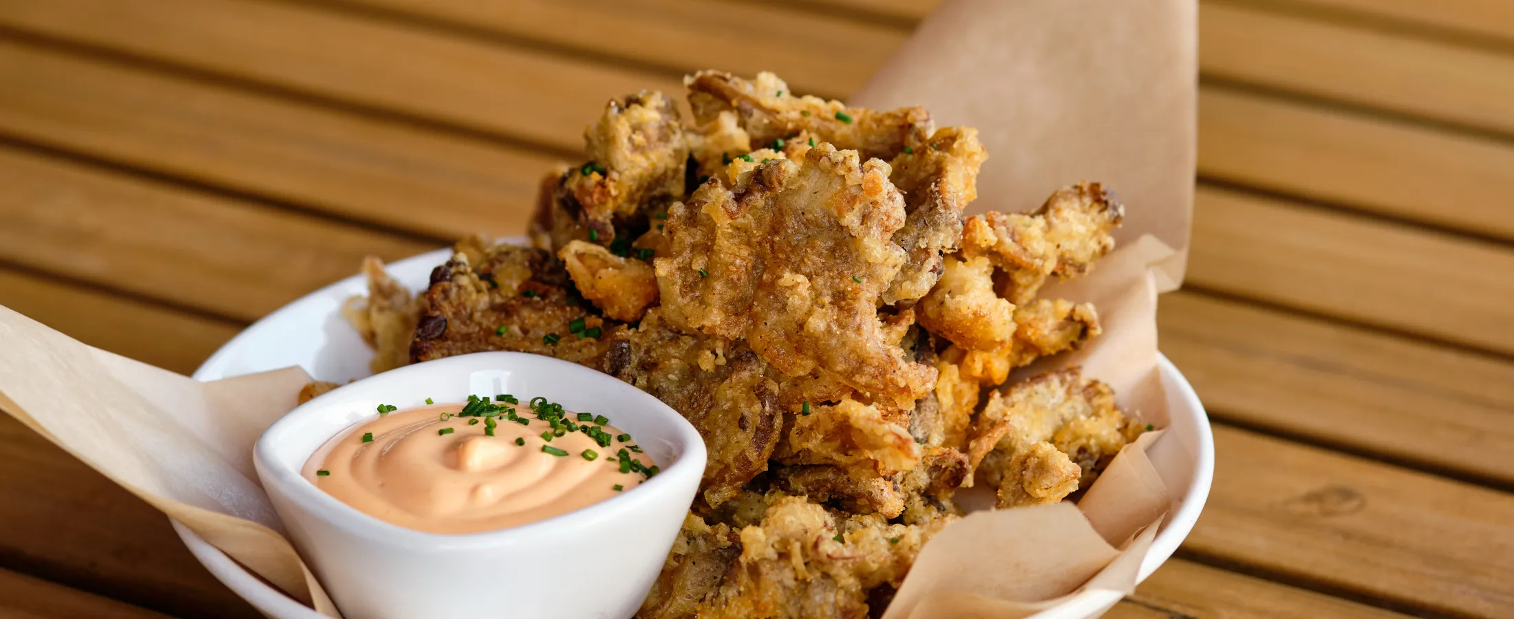 Crispy fried mushrooms served with a creamy dipping sauce garnished with chopped chives on a wooden table.