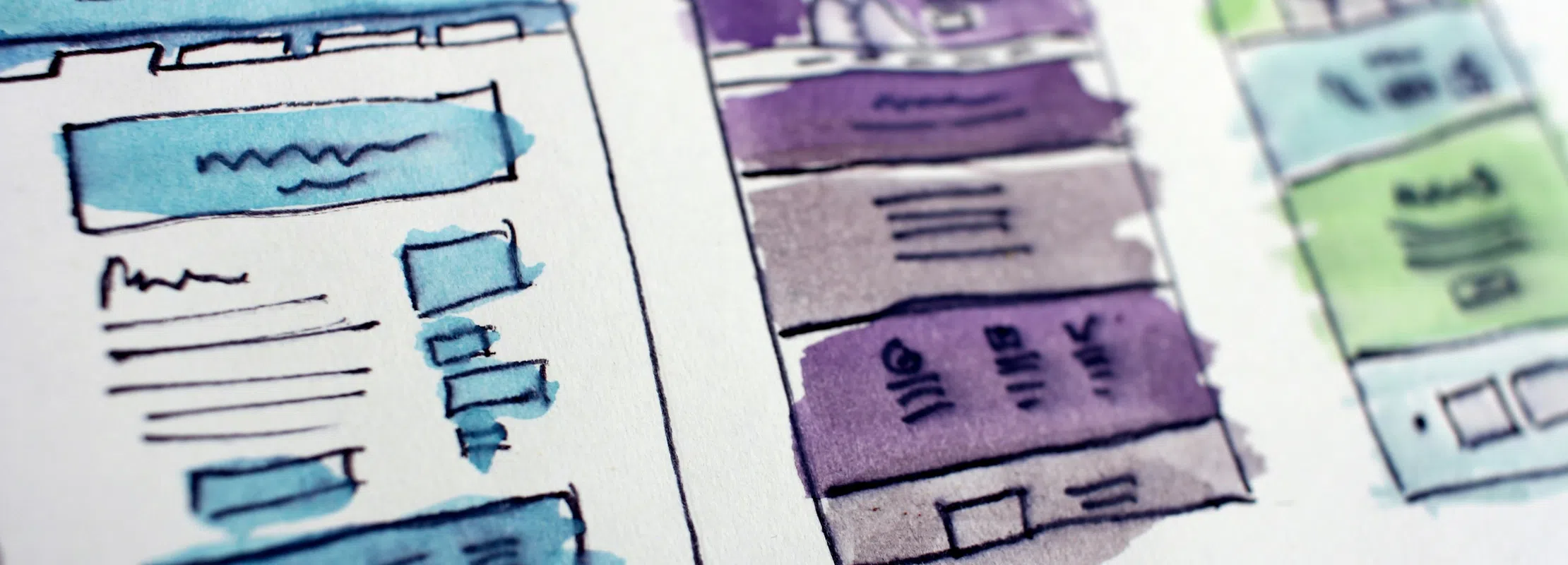 Close-up of three colorful web page wireframe sketches on paper with blue, purple, and green highlights