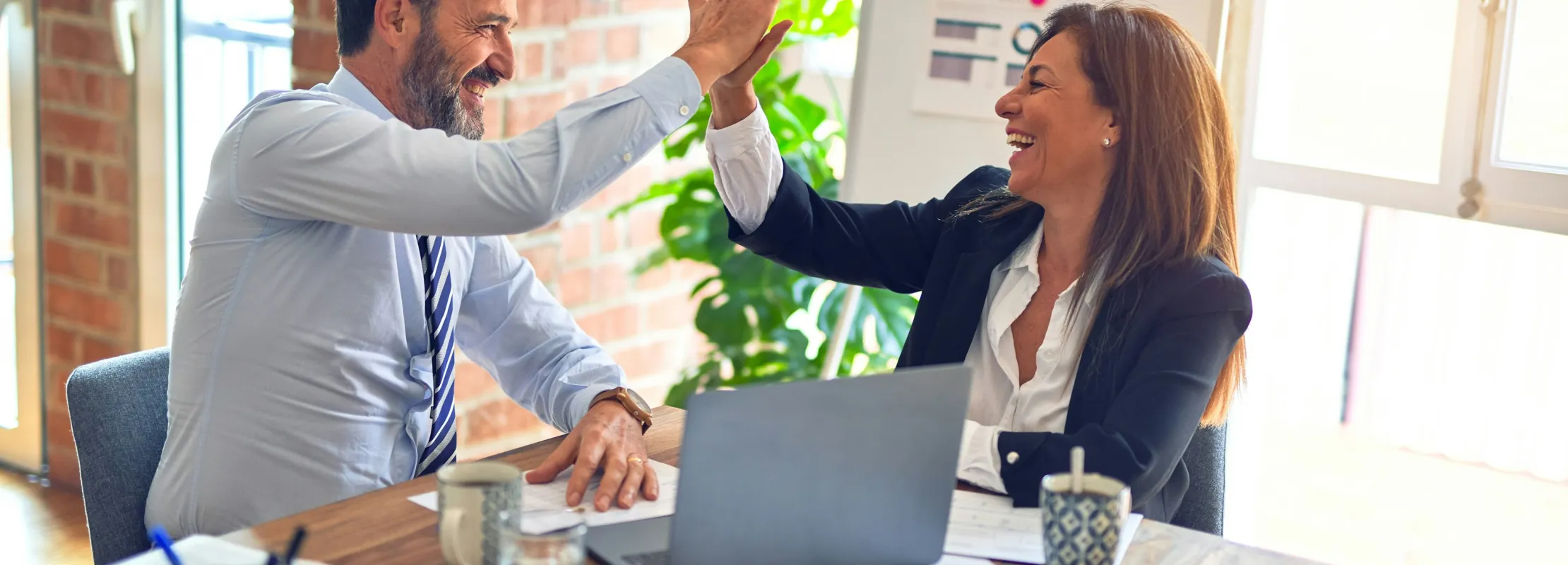Two business colleagues smiling and giving a high-five in a modern office during a meeting.