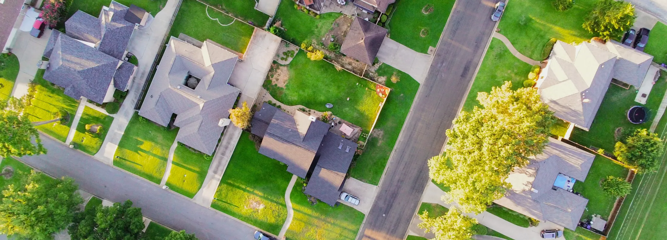 Aerial view of suburban neighborhood with houses, green lawns, and tree-lined streets.