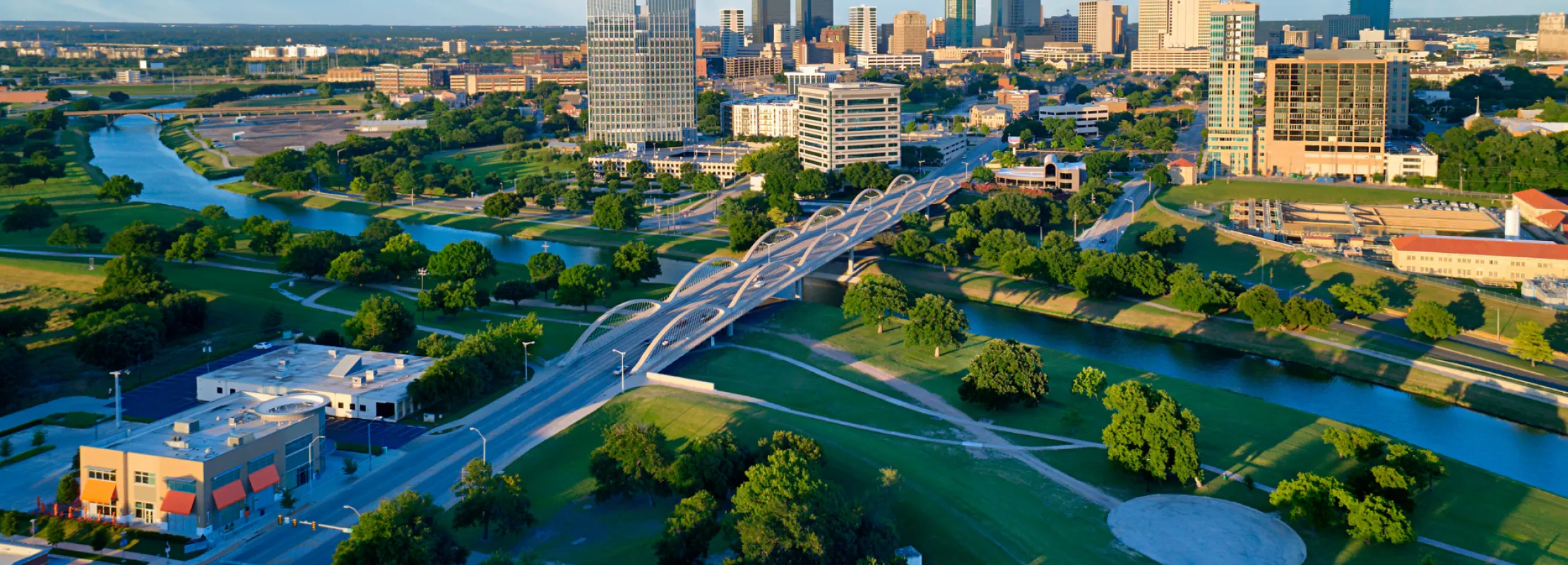 Aerial view of a city skyline with bridges, parks, and a river under a clear blue sky.