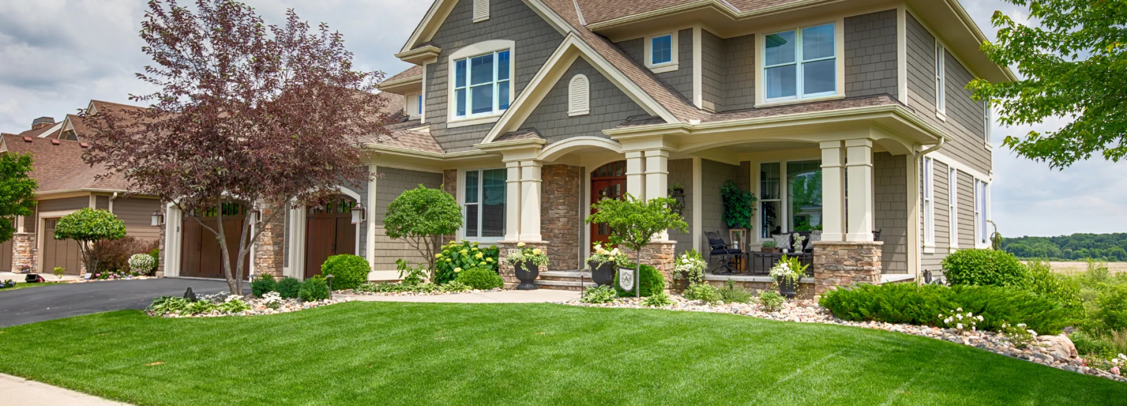 Beautiful suburban home with landscaped yard and trees under a cloudy sky.