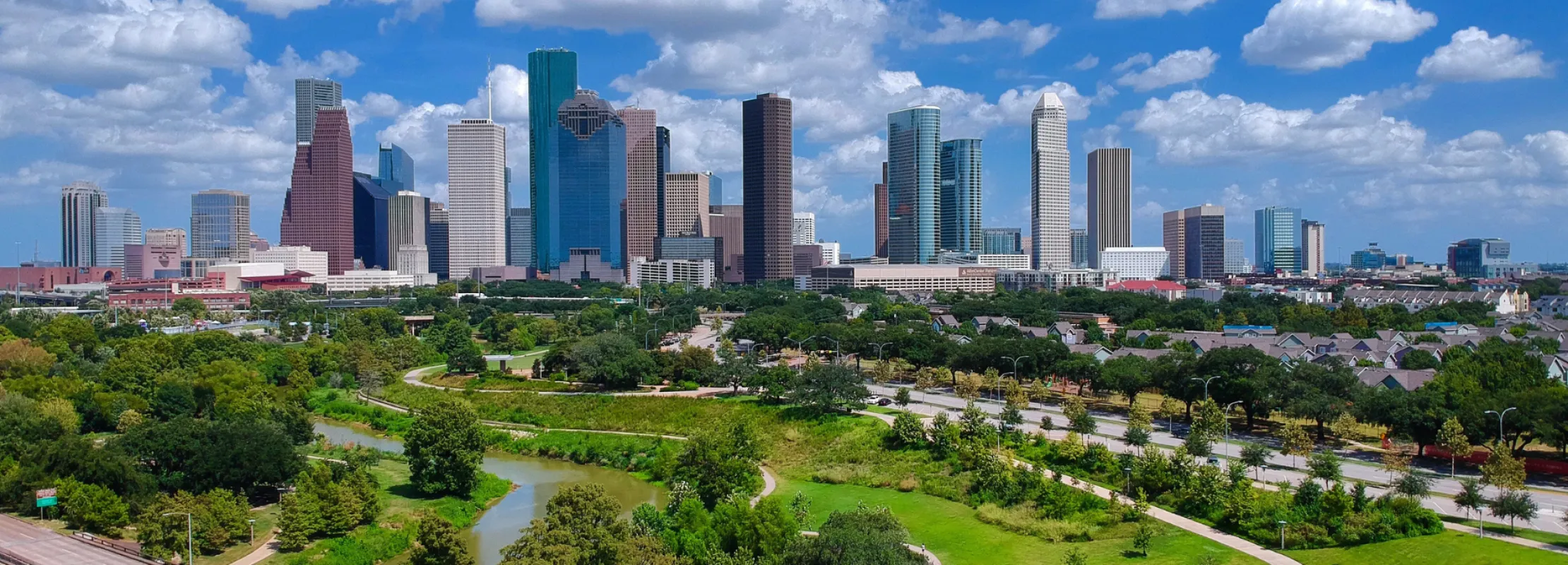 Aerial view of Houston skyline with lush green parks and blue skies in the background.