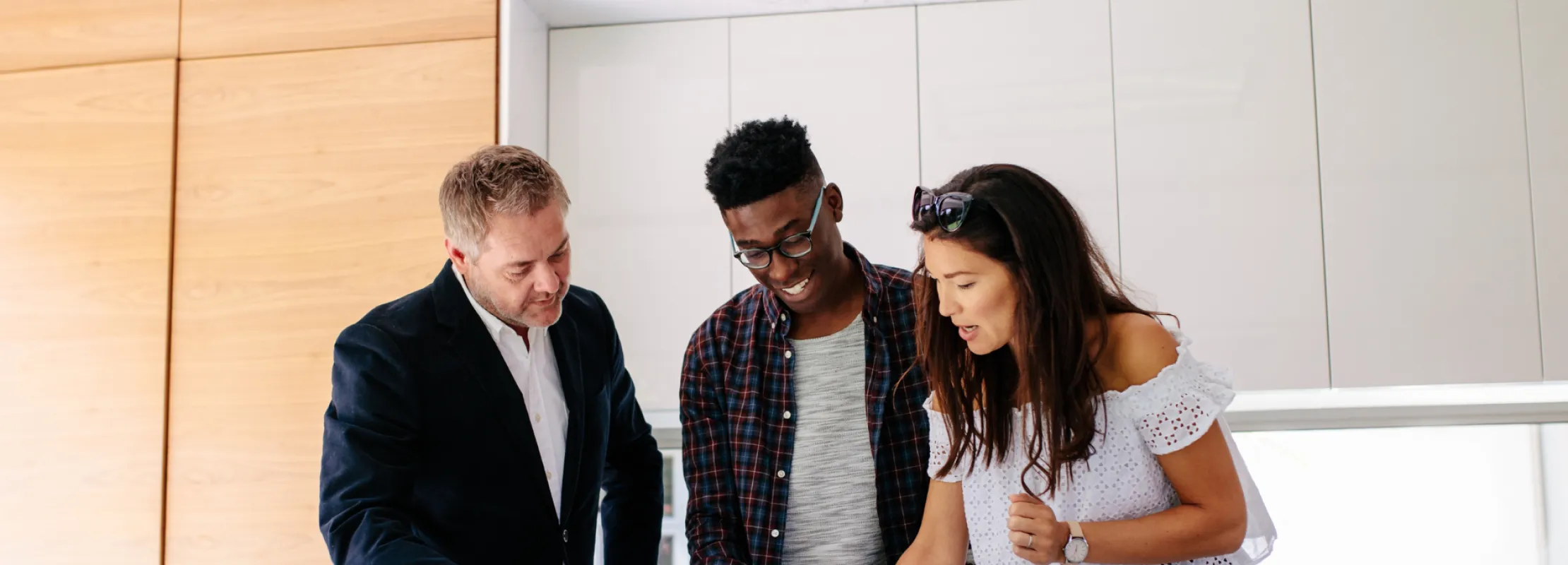 Three diverse professionals collaborating in a modern kitchen space with a notepad and pen.