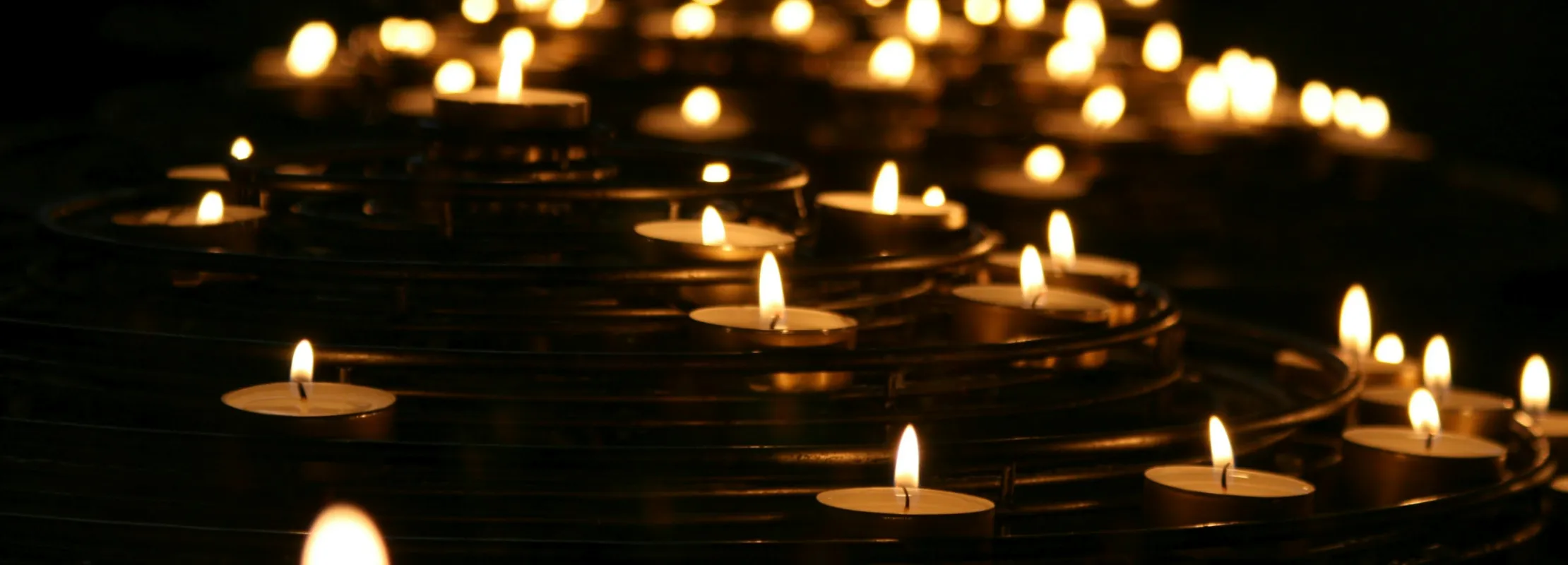 Multiple lit tealight candles arranged in a spiral pattern glowing warmly in dark surroundings