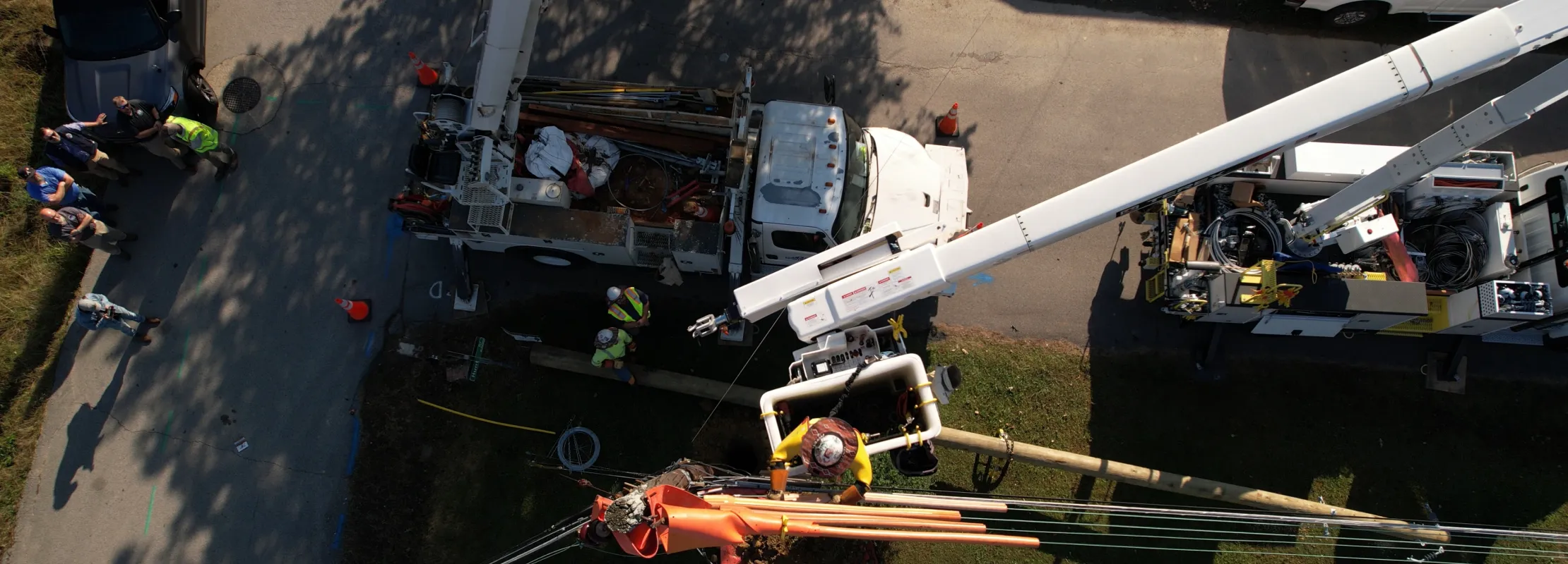Overhead view of utility workers repairing power lines using bucket trucks and safety gear on a sunny day.