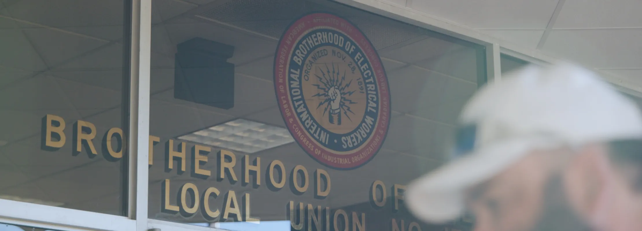 Entrance of Brotherhood of Electrical Workers Local Union with logo on glass door and blurred man in foreground.