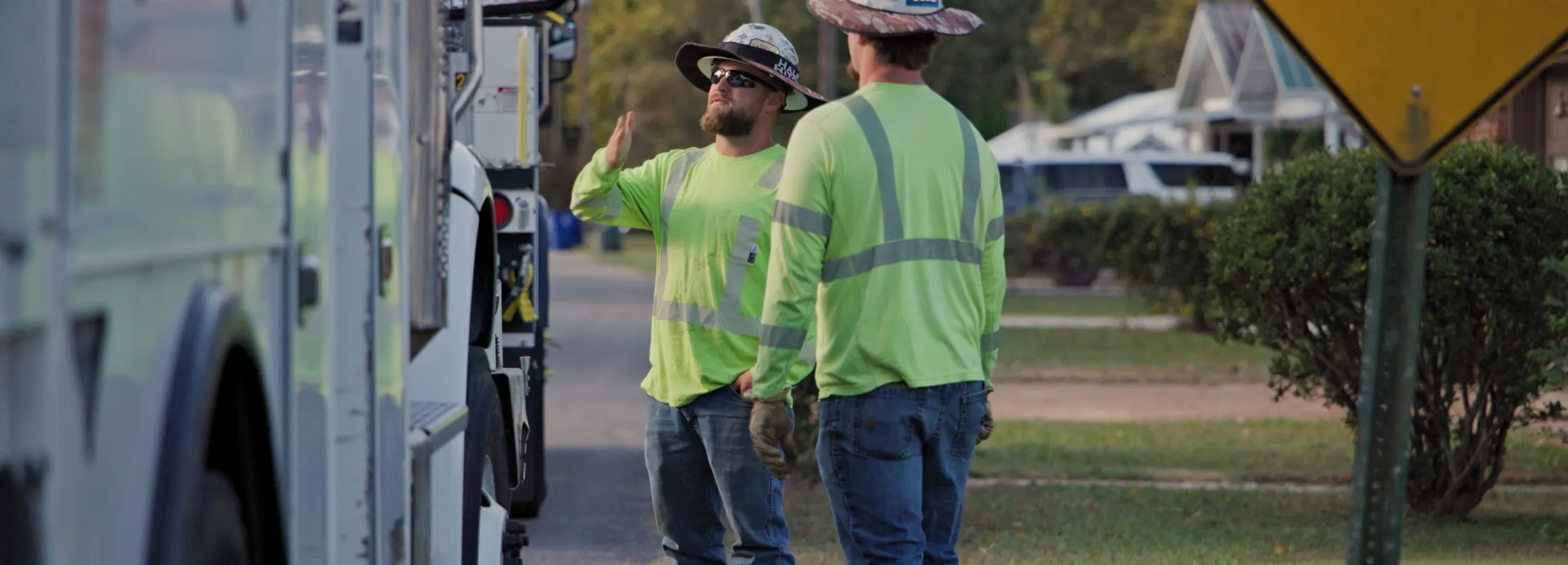 Two utility workers in reflective gear talking beside a utility truck near a street with an end sign