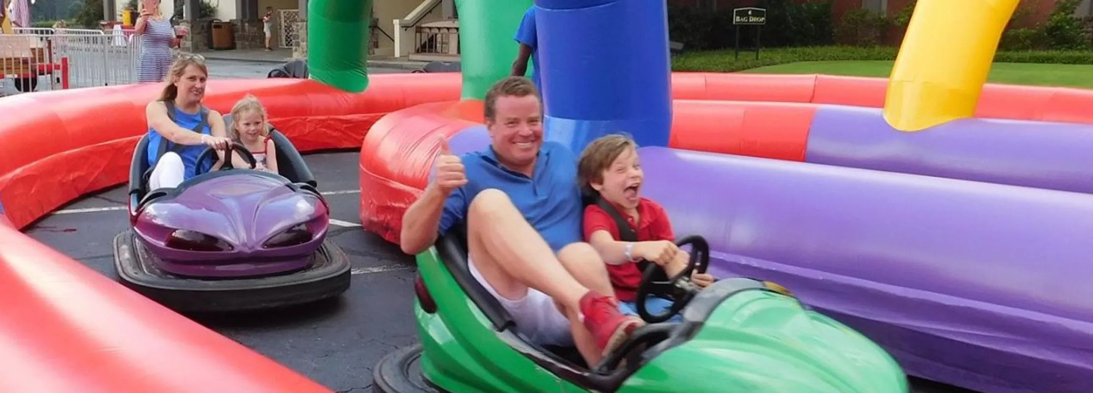 Father and child enjoying a bumper car ride on a colorful inflatable track at an outdoor amusement event.