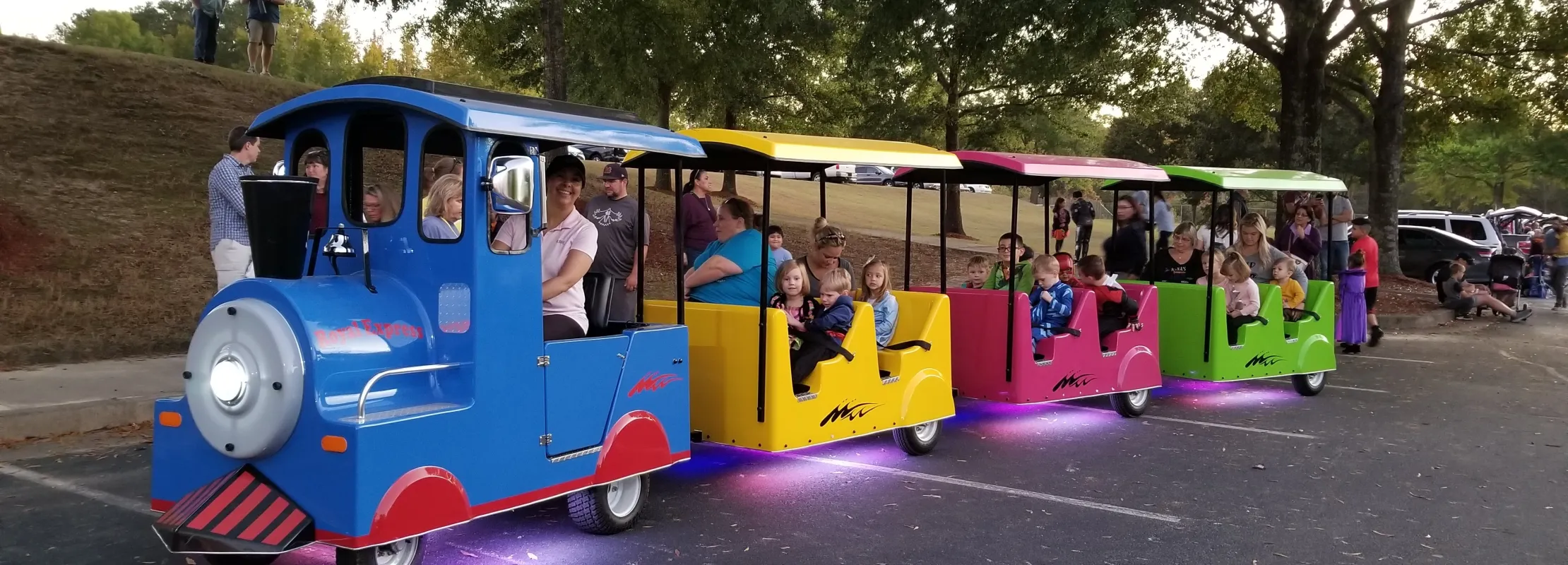 Colorful outdoor train ride with children and adults enjoying evening in park, with purple underglow lights