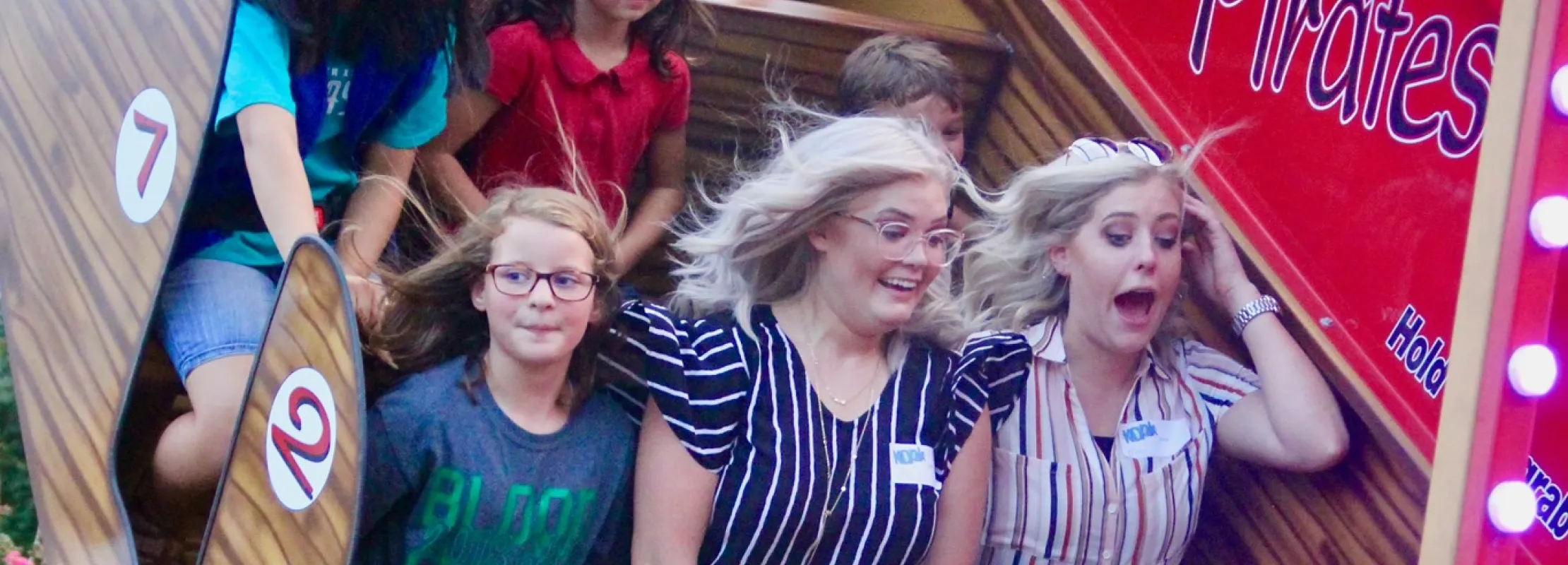 Group of children and adults enjoying a pirate ship amusement park ride with expressions of excitement and joy.