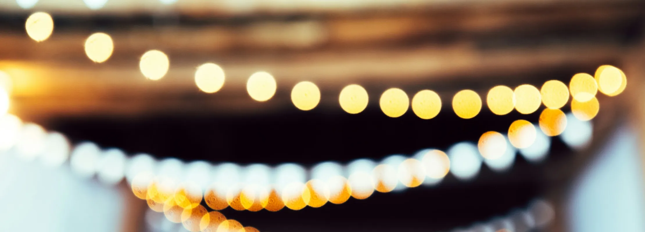 Blurred decorative string lights and triangular bunting hanging from a wooden ceiling at an event space.