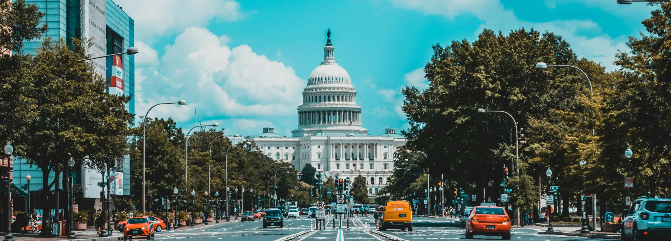 Wide street leading to the United States Capitol with bike lanes and cars under a partly cloudy sky.