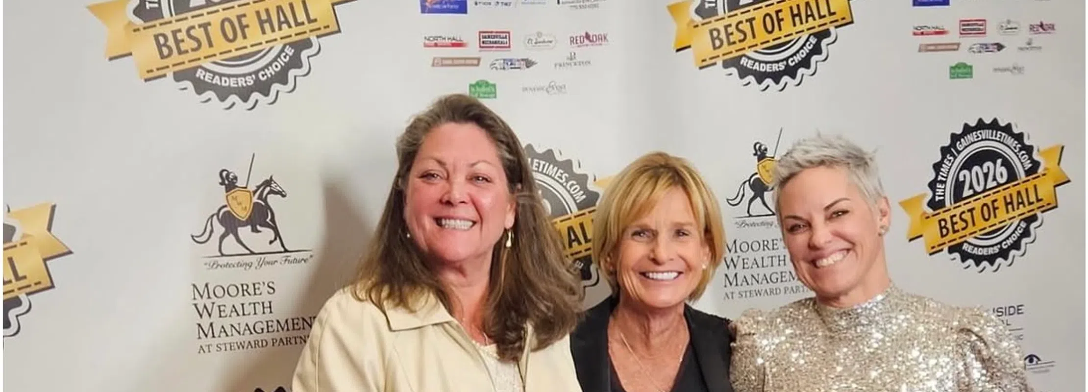 Three women smiling and holding 2026 Best of Hall award plaques at a recognition event backdrop.