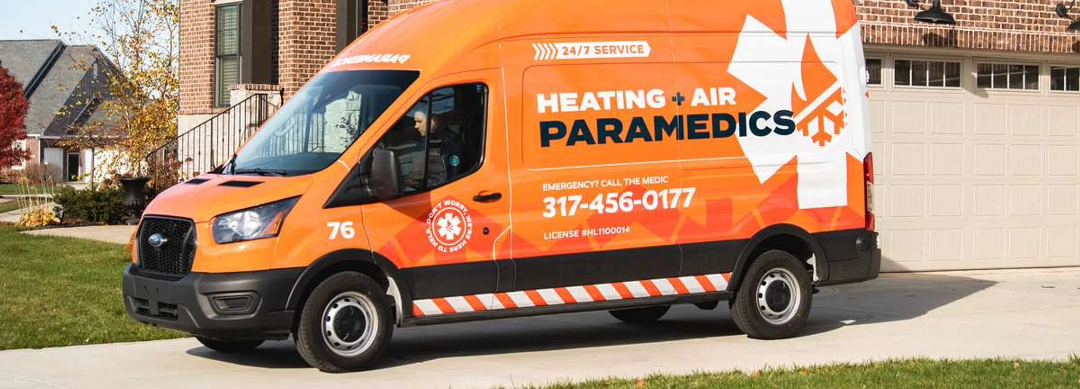 Orange Heating and Air Paramedics service van parked in front of a suburban brick house on driveway.