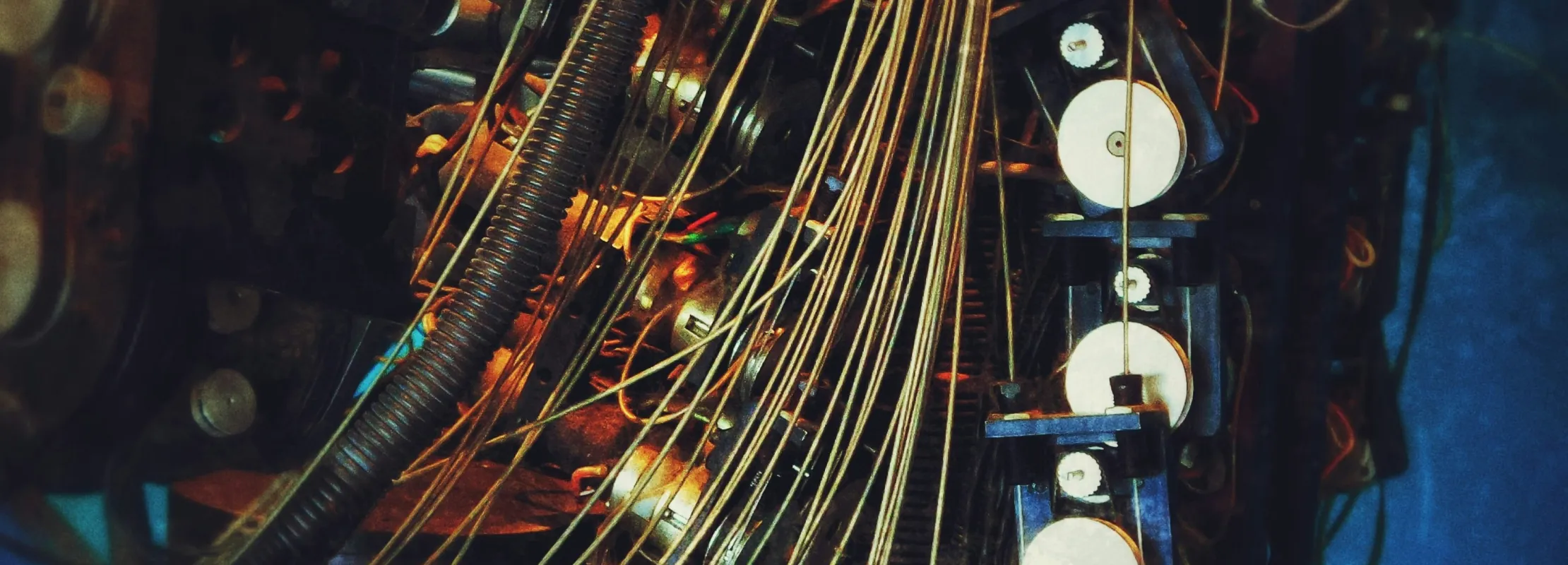 Close-up of vintage mechanical device with multiple wires and pulleys in dim lighting with blue background.