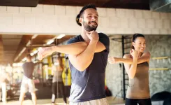 Man and woman stretching arms before workout in bright gym with mirrors and equipment