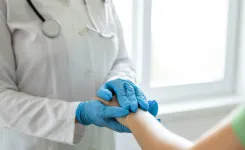 Doctor wearing gloves holding patient's hand gently during a medical consultation in bright clinic.