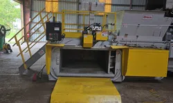 Thumbnail control image for Industrial yellow waste compactor machine inside a warehouse with safety railings and control panel.