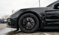 Thumbnail control image for Close-up of a black sports car wheel and tire with multi-spoke rim on a wet asphalt surface