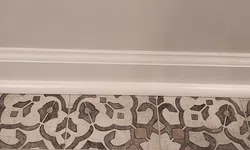 Thumbnail control image for Decorative floor tiles with intricate black and brown floral patterns set against a white base beneath a plain beige wall.