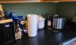 Thumbnail control image for Kitchen countertop with microwave, paper towel roll, knife block, toaster, and wooden cabinets.