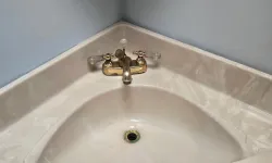 Thumbnail control image for Corner bathroom sink with beige countertop and brass faucet against light gray walls