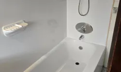 Thumbnail control image for Clean white bathtub with silver faucet and handheld showerhead in a small bathroom with hexagon tile floor.