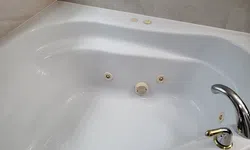 Thumbnail control image for Clean white corner jetted bathtub with chrome faucet and beige marble surround in a bathroom.