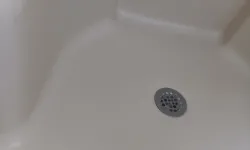 Thumbnail control image for Close-up view of a white bathtub corner with a silver drain and smooth surface.