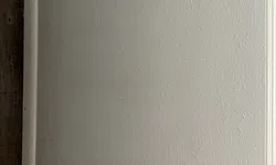 Thumbnail control image for Close-up of a textured beige wall meeting dark wooden flooring and white baseboard trim in a corner.