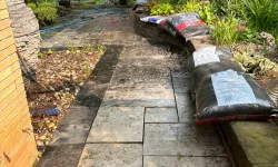 Thumbnail control image for Stone patio with bags of mulch, garden hose, plants, rake, and a white garden arch in a lush backyard.