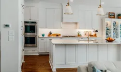 Thumbnail control image for Bright modern white kitchen with large island, wooden floors, stainless steel oven, and pendant lights