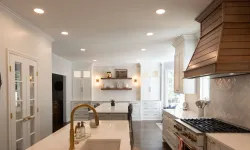 Thumbnail control image for Modern white kitchen with marble countertops, wooden range hood, brass fixtures, and open shelving with decor.