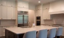 Thumbnail control image for Modern kitchen with white cabinets, large marble island, stainless steel fridge, and four upholstered bar stools.