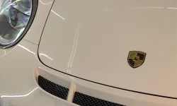 Thumbnail control image for Close-up of a white Porsche sports car hood and headlight with emblem in a garage setting