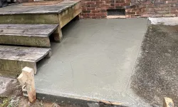 Thumbnail control image for Freshly poured concrete slab beside wooden steps leading to a brick house's back door.