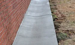 Thumbnail control image for Long freshly poured concrete drainage channel alongside a red brick wall with grass on one side.