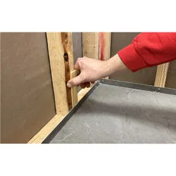 Hand placing small wooden shim between wall studs for alignment during construction.