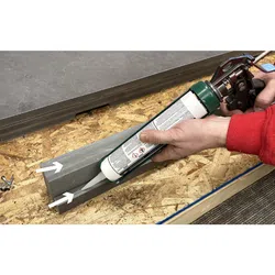 Person applying adhesive with caulking gun inside a gray wooden groove on a workbench.