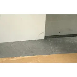 Close-up of marble and gray stone tiles meeting cardboard edge on floor with white and gray wall surfaces