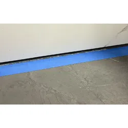 Blue painter's tape applied at the base of a white wall above a gray marble floor during room preparation.