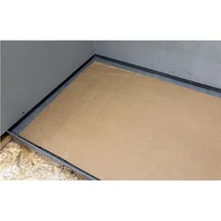 Corner of an unfinished room with a cardboard sheet on the floor next to exposed plywood and gray walls.