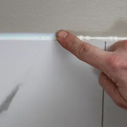 Close-up of finger smoothing fresh white tile adhesive above marble tile on wall during installation