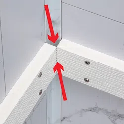 Closeup of white wooden frame corner joint with screws and red arrows on marble tile background